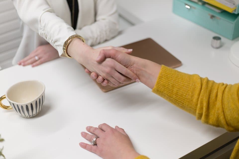 Two people shaking hands across a desk after an interview