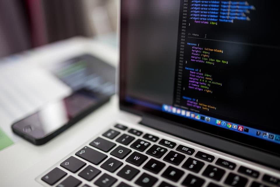 Laptop showing code next to a phone on a desk
