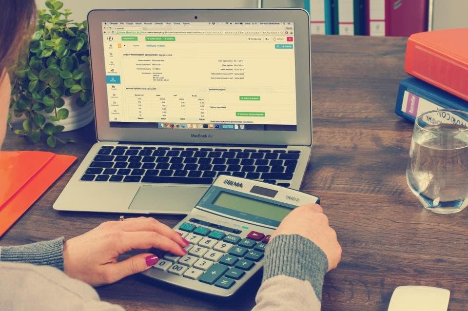 Hands using a calculator beside a laptop spreadsheet