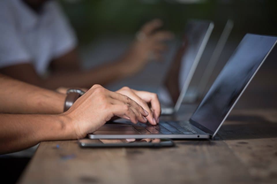 Close-up of hands working on laptops at a wooden desk